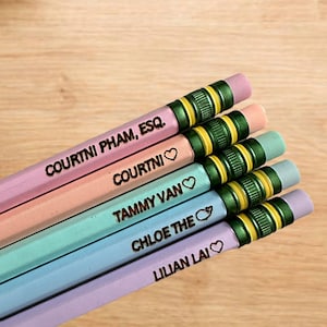 Puede incluir: Un conjunto de seis lápices personalizados con madera pintada de colores vivos y detalles en verde y dorado. Los lápices están etiquetados con los nombres "Courtni Pham, Esq.", "Courtni", "Tammy Van", "Chloe The", "Lillian Lai" y un símbolo de corazón.
