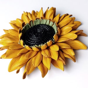 Puede incluir: Un broche de girasol de cuero amarillo con un centro negro y detalles verdes.