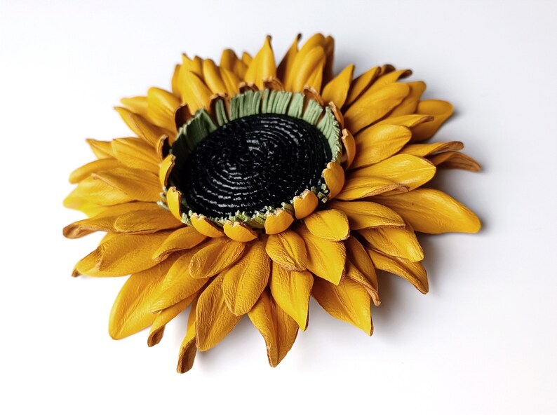 Puede incluir: Un broche de girasol de cuero amarillo con un centro negro y detalles verdes.