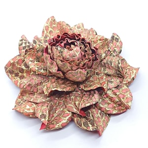 May include: A decorative flower with a layered petal design. The petals feature a scale-like pattern in pink, gold, and brown. The flower's centre is a deep red, providing a striking contrast to the other colours.