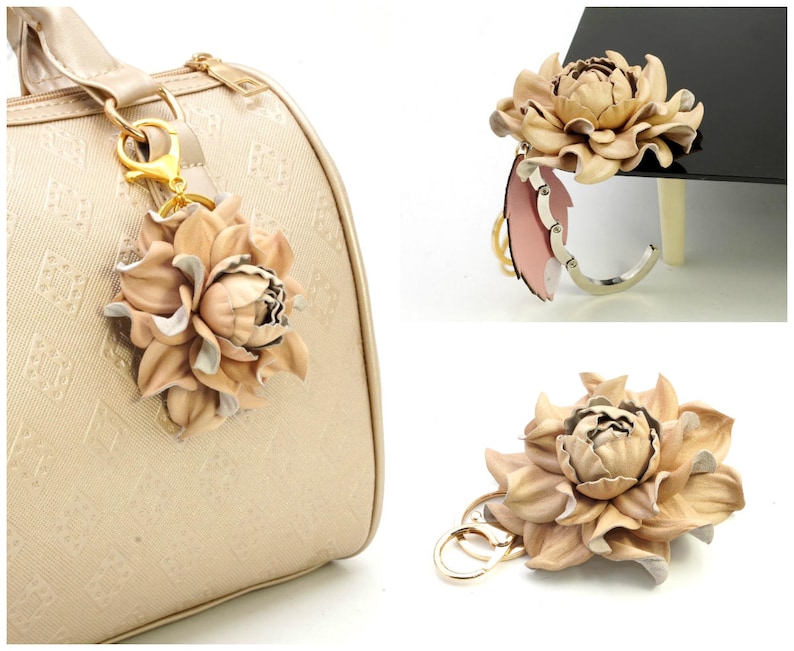 May include: A beige leather flower keychain with gold-colored hardware. The flower has multiple layers of petals and is attached to a gold-colored clasp. The keychain is shown attached to a beige handbag.