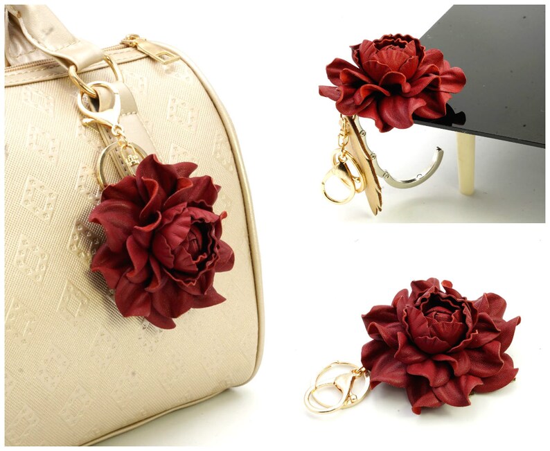 May include: A burgundy leather flower keychain with gold-colored hardware. The flower is a detailed peony shape, and the keychain is attached to a gold-colored purse. The background is white.