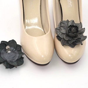 K&ouml;nnte beinhalten: Ein Paar beigefarbene Pumps mit schwarzen Lederblumenverzierungen. Ein Schuh hat eine Blume an der Spitze und der andere eine separate Blume.