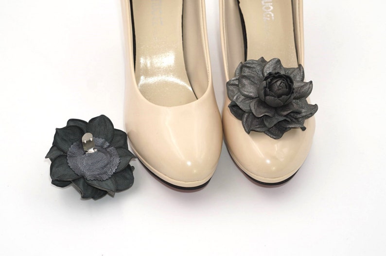 K&ouml;nnte beinhalten: Ein Paar beigefarbene Pumps mit schwarzen Lederblumenverzierungen. Ein Schuh hat eine Blume an der Spitze und der andere eine separate Blume.
