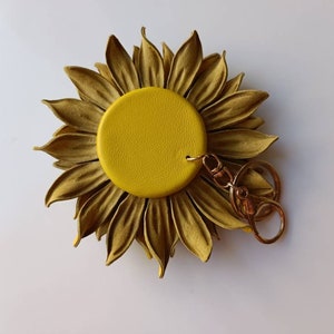 Puede incluir: Un llavero de girasol de cuero amarillo con un anillo y un cierre de metal dorado.