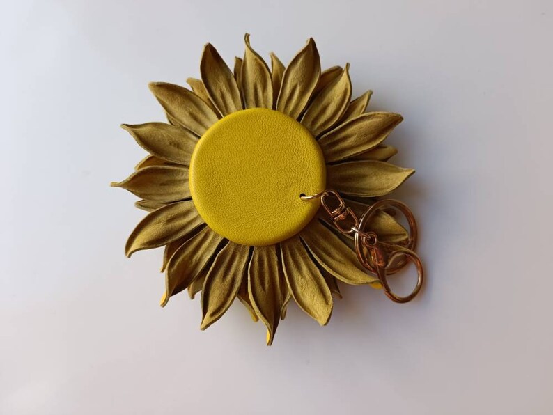 Puede incluir: Un llavero de girasol de cuero amarillo con un anillo y un cierre de metal dorado.