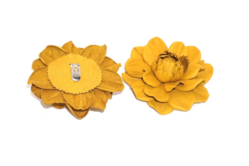 May include: Two yellow leather flower brooches. One brooch is shown from the back, revealing a metal clip. The other brooch is shown from the front.