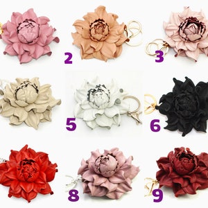 May include: A collection of nine leather flower keychains in various colors, including pink, tan, white, black, red, and burgundy. Each keychain features a detailed floral design with a gold or silver-tone keyring.