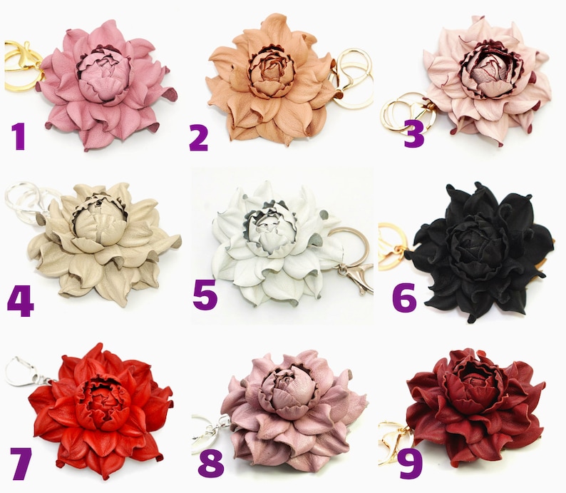 May include: A collection of nine leather flower keychains in various colors, including pink, tan, white, black, red, and burgundy. Each keychain features a detailed floral design with a gold or silver-tone keyring.