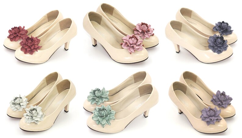 Op de afbeelding: Zes paar cr&egrave;mekleurige pumps met kleine hakken, elk versierd met een grote stoffen bloem. De bloemen zijn er in verschillende kleuren, waaronder bordeauxrood, roze, blauw, wit en lavendel, wat een scala aan keuzes biedt.