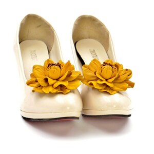May include: A pair of white shoes with yellow flower embellishments. The flowers are made of leather and have a realistic appearance.
