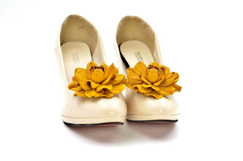 May include: A pair of white shoes with yellow flower embellishments. The flowers are made of leather and have a realistic appearance.