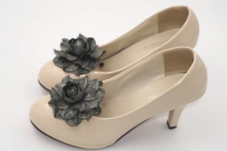 K&ouml;nnte beinhalten: Ein Paar beigefarbene High-Heel-Schuhe mit schwarzen Stoffblumenverzierungen.