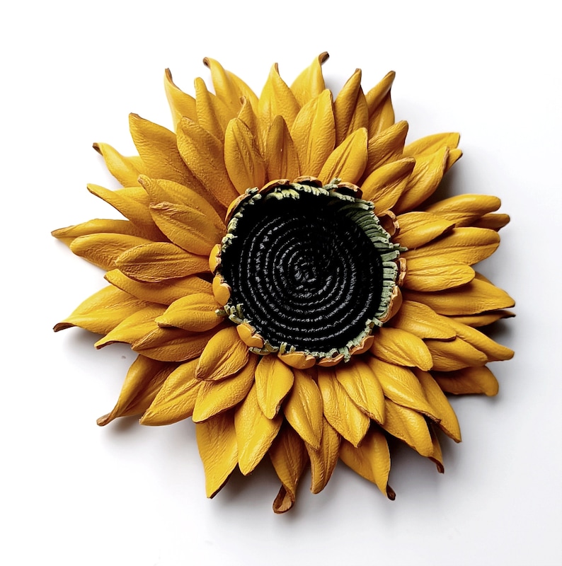Puede incluir: Un gran girasol de cuero amarillo con un centro negro. El girasol est&aacute; hecho de p&eacute;talos de cuero individuales y tiene un aspecto realista.