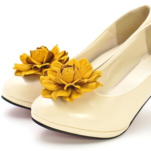 May include: A pair of cream-colored high-heeled shoes with yellow flower embellishments.