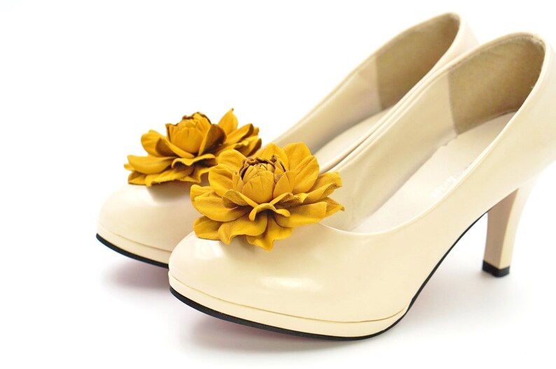 May include: A pair of cream-colored high-heeled shoes with yellow flower embellishments.