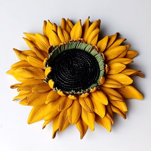 Puede incluir: Un broche de girasol de cuero amarillo con un centro verde. El girasol est&aacute; hecho de p&eacute;talos individuales cosidos juntos.