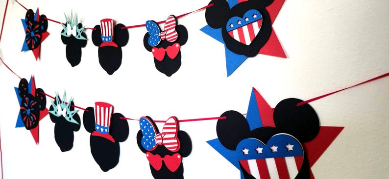 May include: A festive banner featuring black Mickey Mouse silhouettes with patriotic red, white, and blue accents. The banner includes stars, hearts, and bows, perfect for a themed celebration.