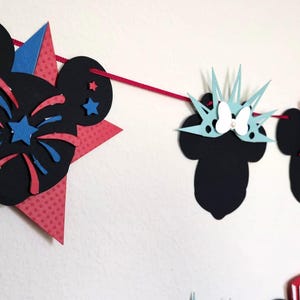 May include: A festive banner featuring Mickey Mouse silhouettes and star shapes in red, white, and blue. The banner includes designs of fireworks, the Statue of Liberty, and Uncle Sam hats, perfect for patriotic celebrations.