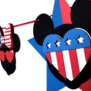 May include: A patriotic garland featuring Mickey Mouse-shaped cutouts in red, white, and blue. The garland includes stars, hearts, and bowties, perfect for Independence Day or other festive occasions. The design incorporates the colors of the American flag.