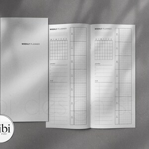 May include: A white weekly planner with a black grid and lines. The planner has two pages, each with a weekly layout. The planner is closed and has a white cover with the text "WEEKLY PLANNER" printed in black.