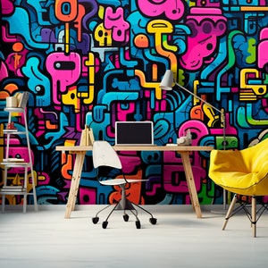 May include: A modern office space featuring a vibrant, colorful graffiti art wall. The room includes a wooden desk with a laptop, a white chair, and a yellow armchair. A small bookshelf and artwork are also present, creating a creative workspace.