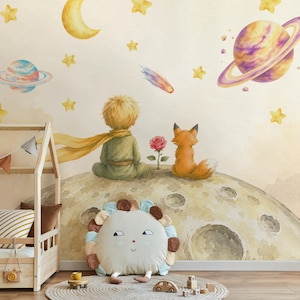May include: A wall mural featuring a watercolor illustration of a young person with blonde hair and a yellow scarf sitting on a cratered moon next to a fox and a single red rose. The background displays a crescent moon, stars, and planets.
