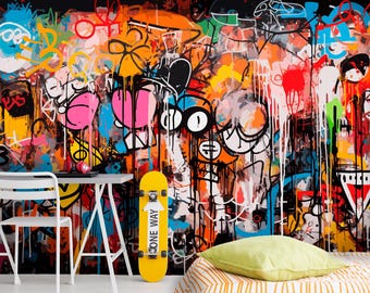 Puede incluir: Un mural de pared vibrante con arte de grafiti caótico con capas de gotas de pintura negra, naranja, rosa, azul y amarilla. Un monopatín amarillo con un gráfico de flecha blanca está apoyado contra la pared cerca de un escritorio y una silla blancos.