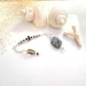 Peut inclure: Un bracelet en chaîne argent avec un pendentif en gros cristal bleu et vert. Le bracelet est orné de petits cristaux bleus et bruns.