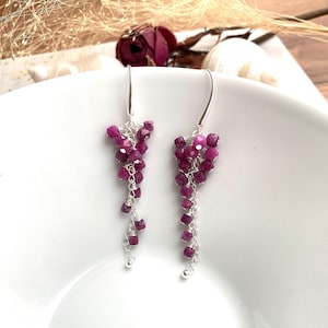 Può includere: Un paio di orecchini pendenti con un gruppo di pietre di rubino rosa appese a una catena d'argento.