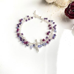 Pode incluir: Um bracelete de prata com um fecho pendente e contas de pedras preciosas roxas e azuis.