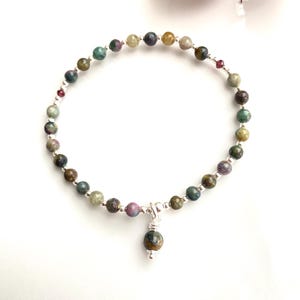 Könnte beinhalten: Ein zartes Armband aus kleinen, mehrfarbigen Edelsteinperlen und einem silbernen Anhänger. Die Perlen sind eine Mischung aus Grün, Braun, Rosa und Gelb.