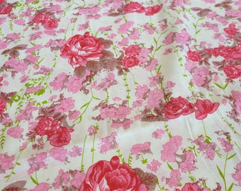 May include: Floral fabric featuring a repeating pattern of large, vibrant pink roses and smaller pink blossoms on a white background. Green stems and leaves add detail to the design. The fabric is suitable for various sewing projects.