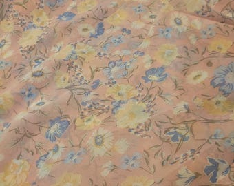 May include: A close-up of a fabric with a floral pattern. The fabric has a light pink background with a repeating pattern of blue and yellow flowers and green stems. The flowers are in various sizes and shapes.