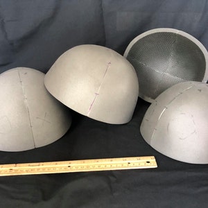 Puede incluir: Cuatro formas de cúpula de espuma gris, tres con marcas y una con un patrón de cuadrícula, sobre una superficie negra con una regla de madera.