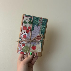 May include: A small, wrapped package with a cat illustration and strawberry-themed decorative paper. The package is tied with twine and sealed with a green wax seal. The overall aesthetic is vintage and whimsical.