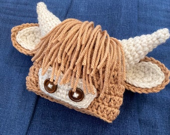 May include: A crocheted brown and white highland cow hat with brown button eyes.
