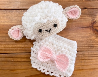 May include: A white crocheted lamb with pink ears and a pink bow. The lamb is wearing a white crocheted outfit.