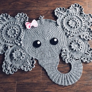 May include: Gray crocheted elephant rug with a pink bow. The elephant's ears are made of crocheted doilies.