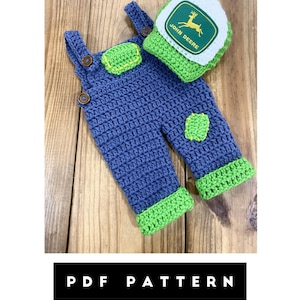 May include: A blue and green crochet baby outfit, including overalls and a hat. The overalls have green accents on the pockets and cuffs, with wooden button closures. The hat features the John Deere logo. The text "PDF PATTERN" is at the bottom.