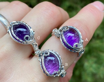 May include: Three silver rings with amethyst gemstones. The rings are wire wrapped and feature a unique design. The rings are labeled A, B, and C.