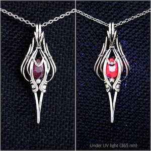 May include: A silver wire-wrapped pendant featuring a faceted dark red gemstone suspended on a silver chain. The right side shows the same pendant under 365 nm UV light, causing the gemstone to fluoresce with a bright, vivid red glow.