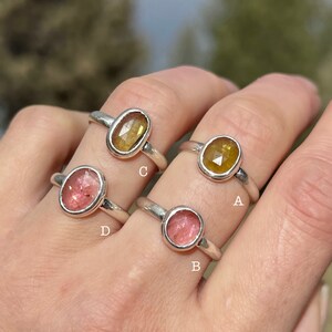 May include: Four silver rings with different colored gemstones. The rings are labeled A, B, C, and D. The gemstones are yellow, pink, and red.