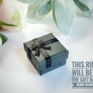 May include: A small gray gift box with a black ribbon and bow. The text "THIS RING WILL BE IN THE GIFT BOX READY TO GIFT!" is printed below the box.
