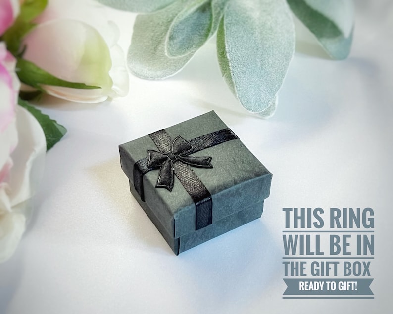 May include: A small gray gift box with a black ribbon and bow. The text "THIS RING WILL BE IN THE GIFT BOX READY TO GIFT!" is printed below the box.