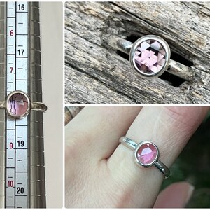 May include: A silver ring with a pink gemstone. The ring is shown on a ring sizer and on a finger.