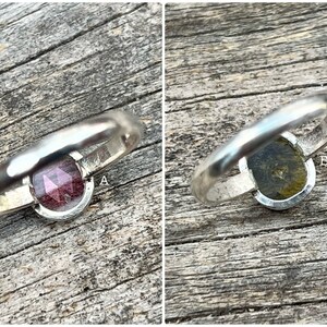 May include: Two silver rings with different gemstones. The ring on the left has a pink gemstone, and the ring on the right has a green gemstone.