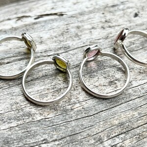 May include: Four silver rings with different colored gemstones. The rings are on a wooden surface.