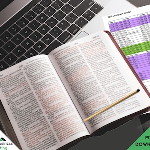 Peut inclure: Une Bible ouverte avec du texte rouge et un crayon posés sur une surface sombre, à côté d'un clavier d'ordinateur portable et d'un calendrier liturgique 2026. Le calendrier comporte des sections codées par couleur et un graphique "PDF DOWNLOAD".
