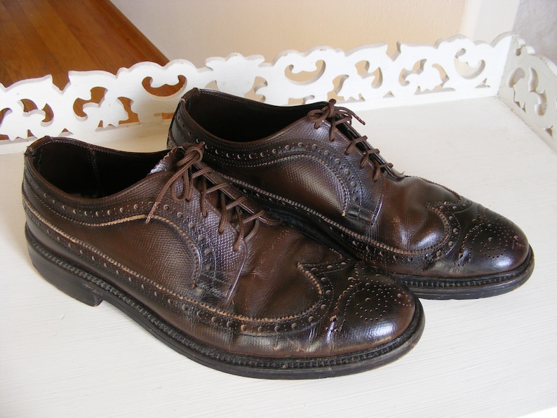 May include: Two brown leather brogue shoes with laces. The shoes have a wingtip design and are on a white surface.